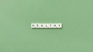 Scrabble tiles spelling the word 'healthy' on a light green background, top view.