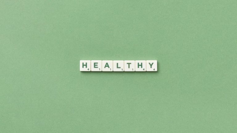 Scrabble tiles spelling the word 'healthy' on a light green background, top view.